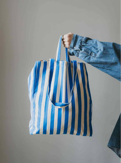 Blue and white striped tote bag held by a person wearing a denim jacket against a plain background
