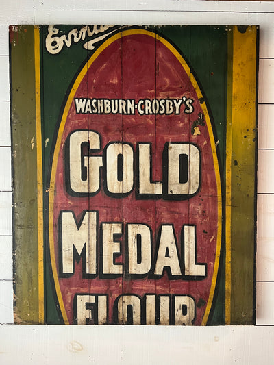 Vintage hand painted gold metal flour sign with red and green accents on a wooden background.
