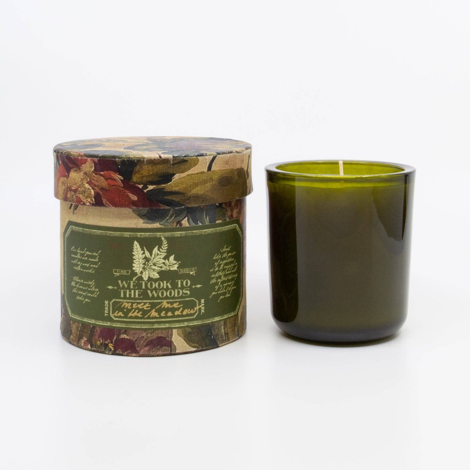Green candle in a decorative box with floral design on a white background. We took to the woods. 