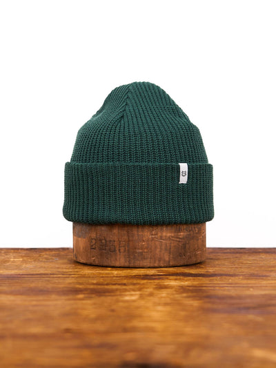 Green knit beanie on a wooden block with a white background