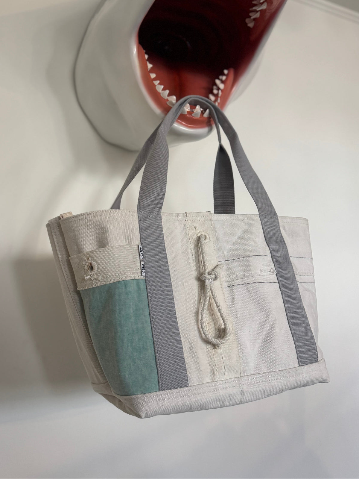 Shark-shaped wall decoration with a handbag hanging from its mouth on a white wall.