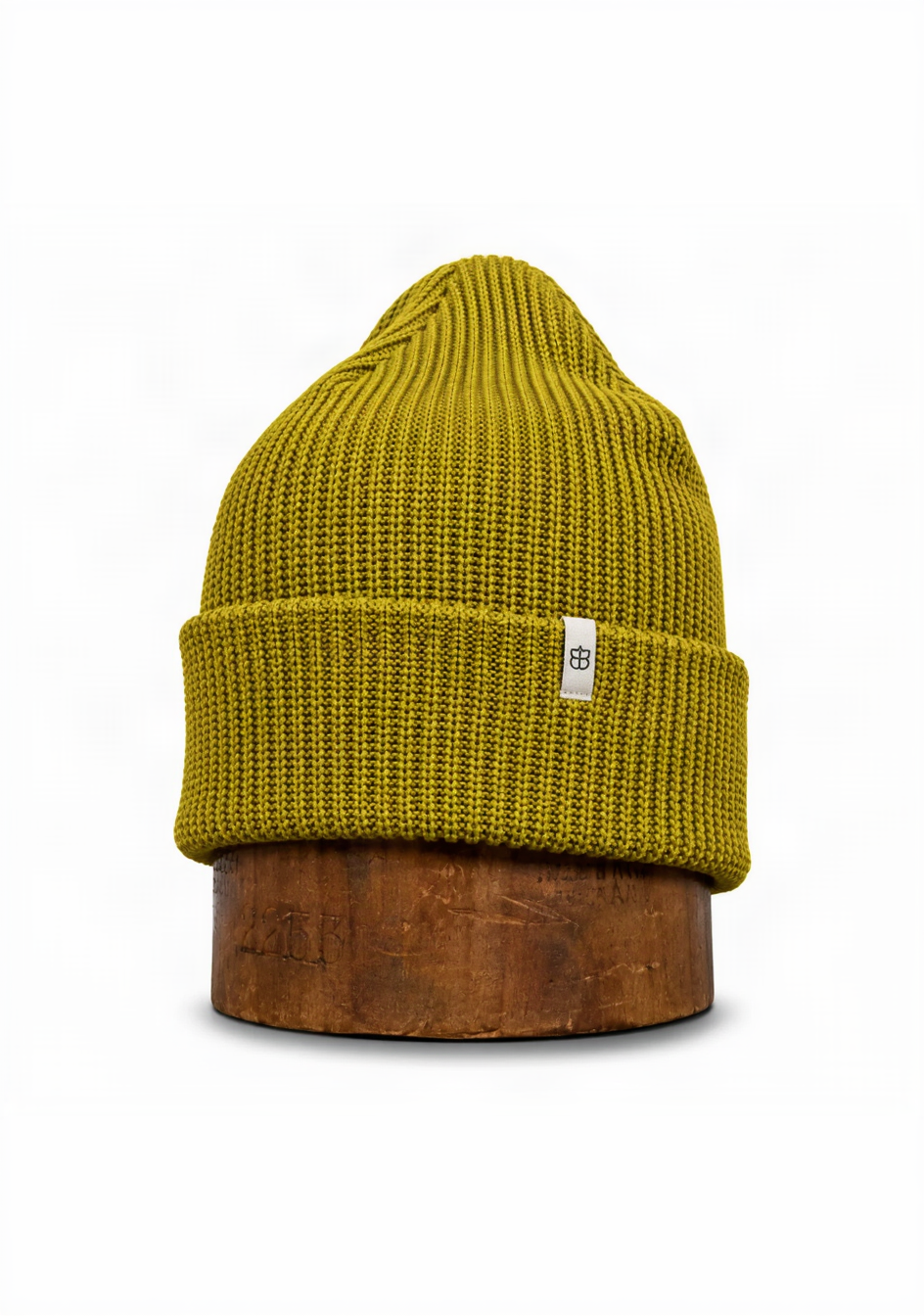 A ribbed knit beanie hat in a mustard yellow color, displayed on a rustic wooden stand against a white background.