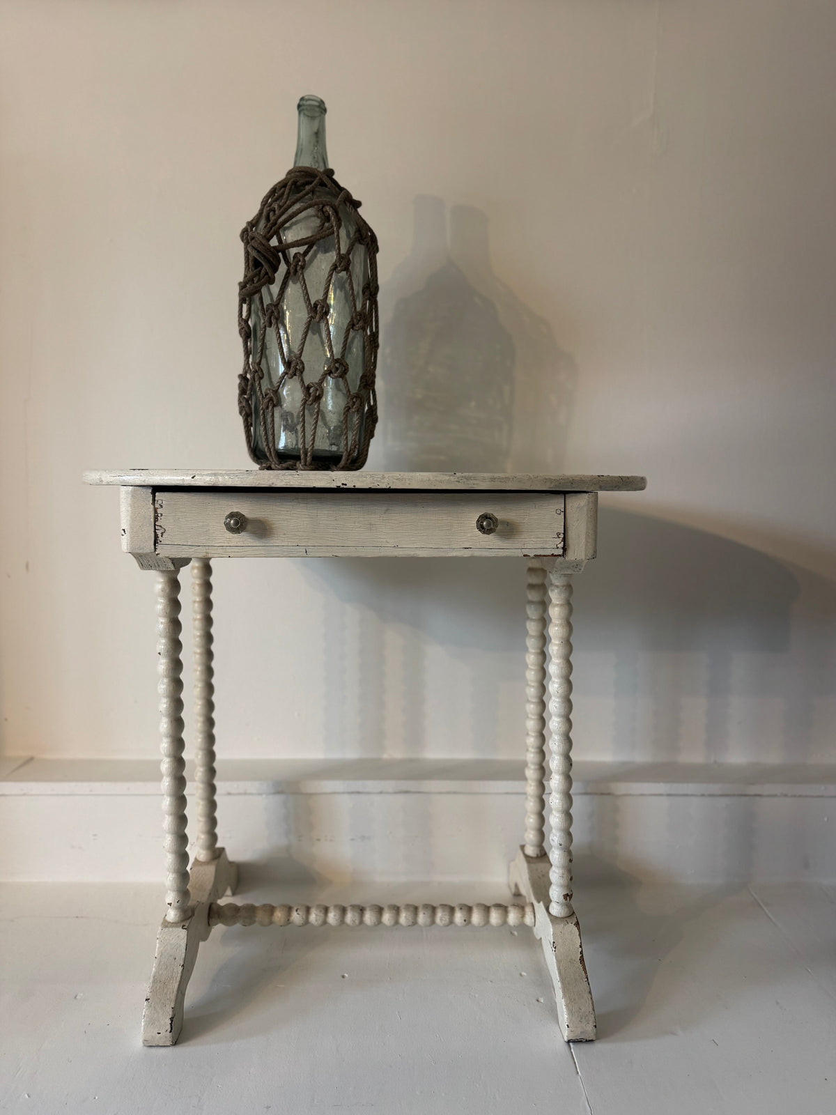 Small  antique painted wooden table with a decorative bottle with knotted rope on a plain background