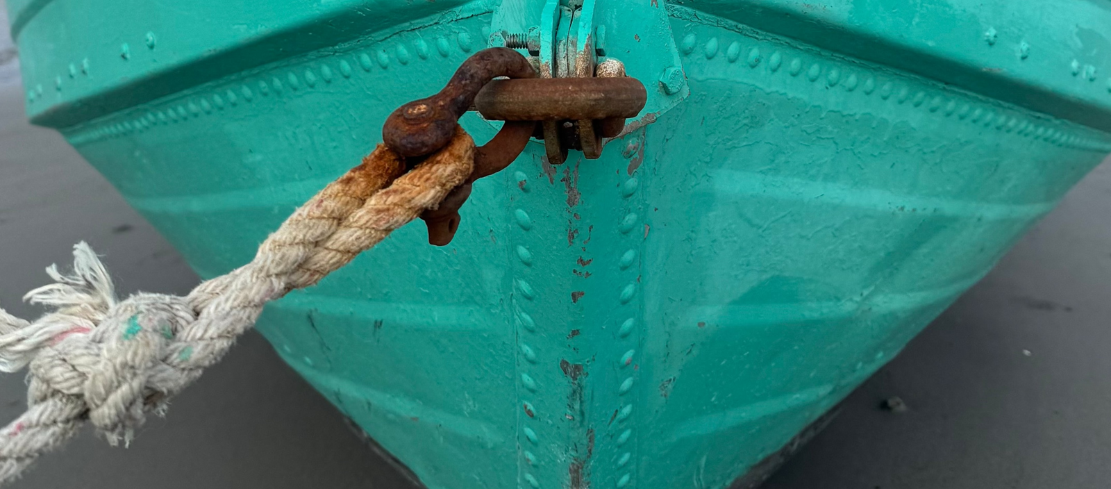 Teal boat with a rope tied to its bow on a gray surface