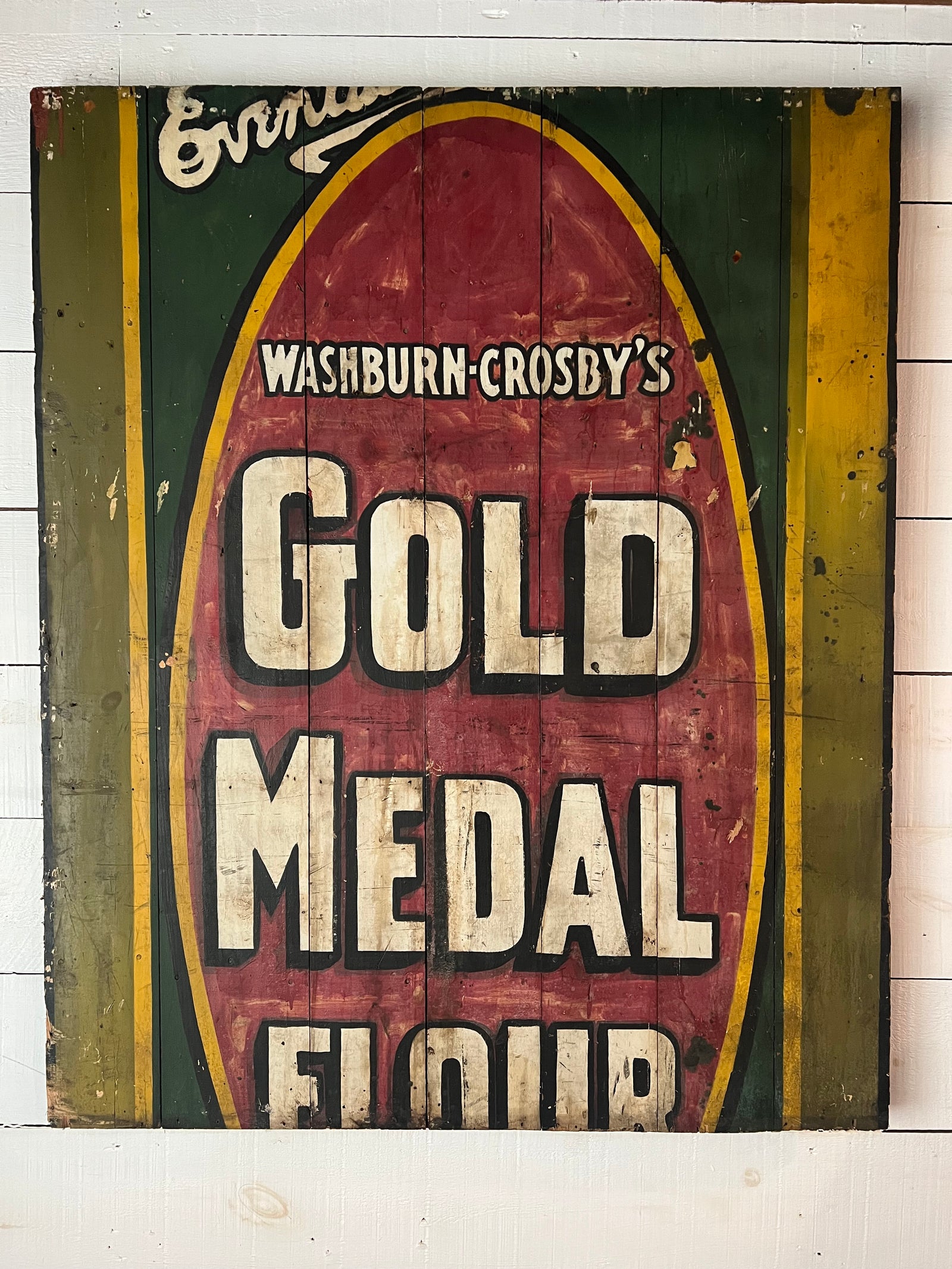 Vintage hand painted gold metal flour sign with red and green accents on a wooden background.