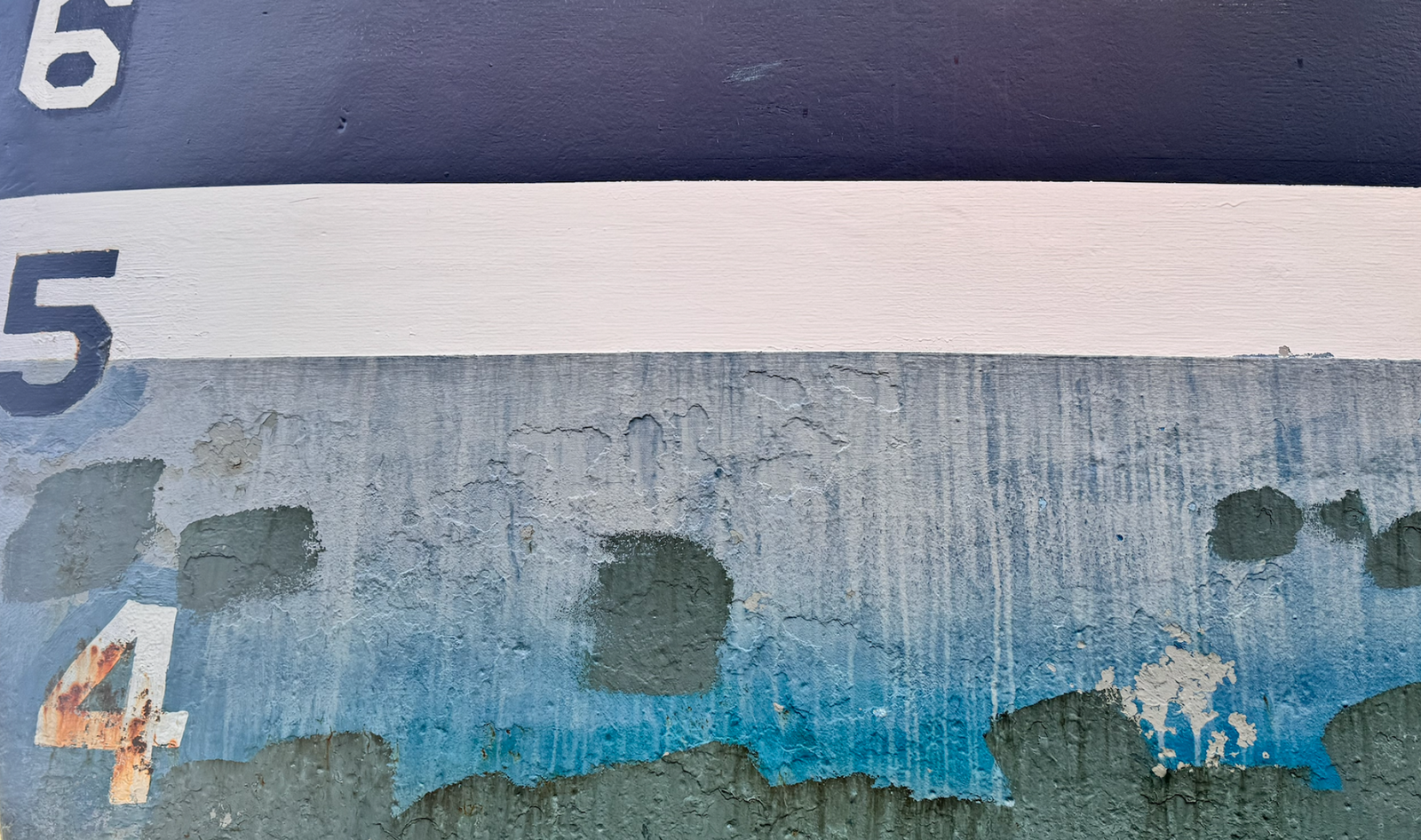 A close-up of a weathered painted surface with the numbers 6, 5, and 4 visible, showing peeling blue, white, gray, and dark green paint.