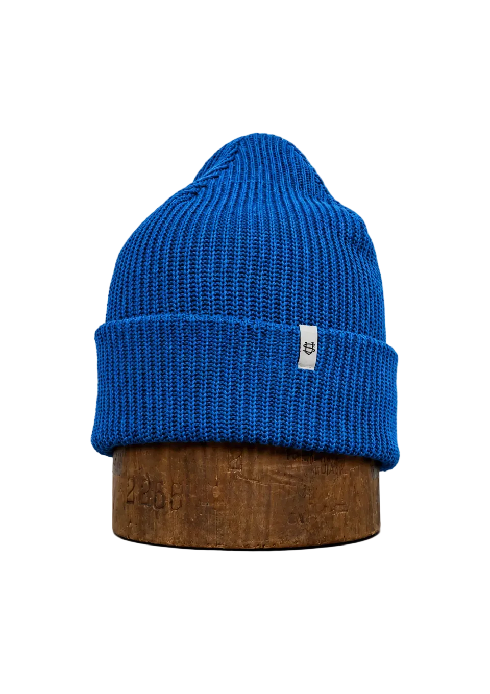 A bright blue ribbed knit beanie hat displayed on a brown wooden stand against a plain white background.